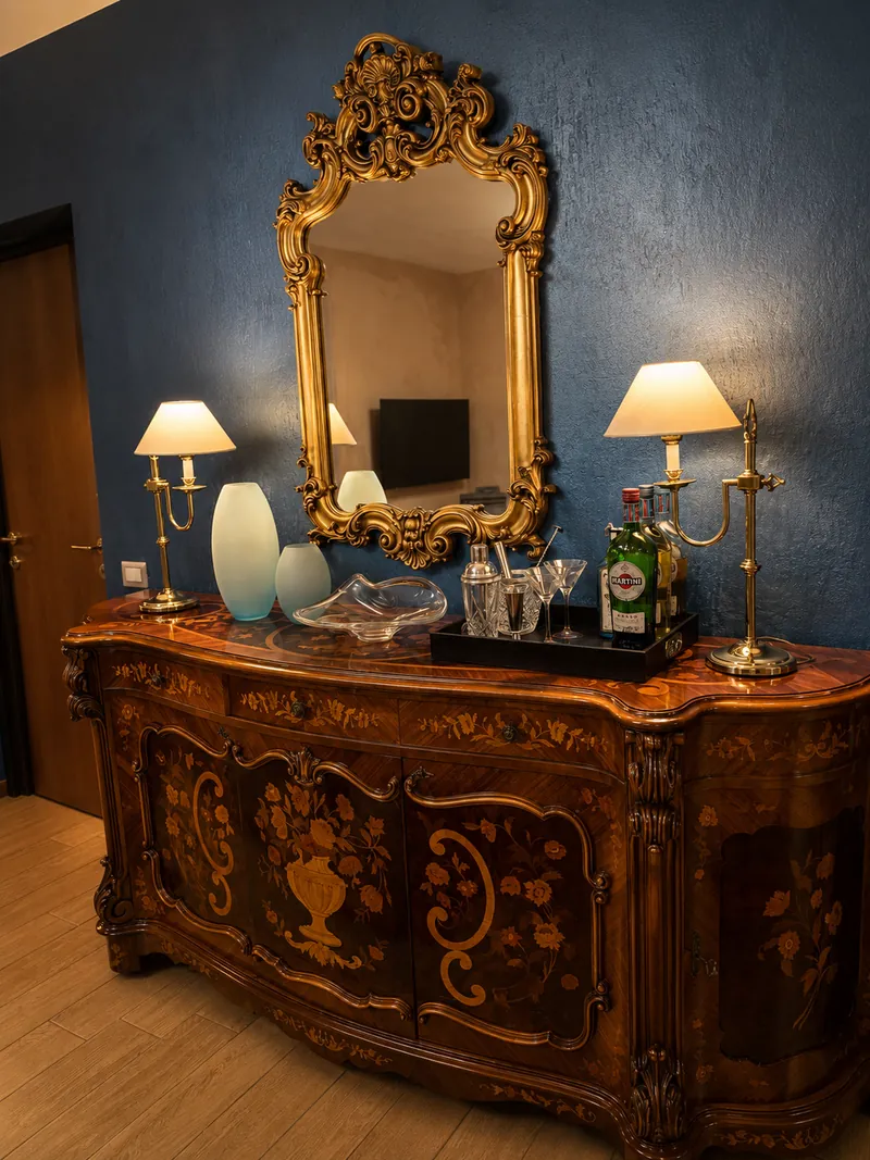 Inlaid wooden sideboard with a gilded mirror, brass lamps and glass vases
